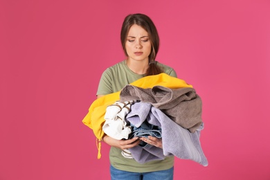 Photo of Displeased young woman holding pile of dirty laundry on color background