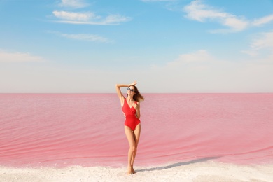 Photo of Beautiful woman in swimsuit posing near pink lake on sunny day