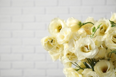 Beautiful white Eustoma flowers near brick wall, closeup. Space for text