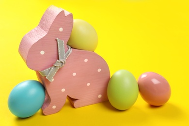 Photo of Cute wooden Easter bunny and dyed eggs on color background