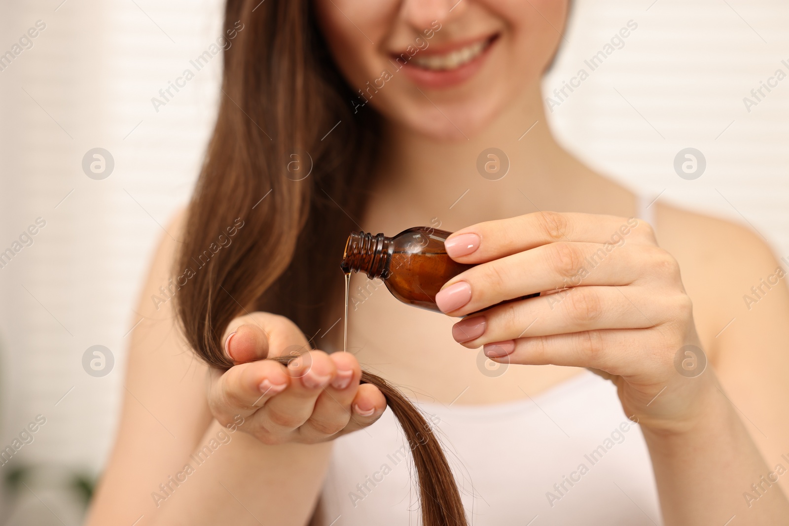 Photo of Woman applying oil hair mask indoors, closeup