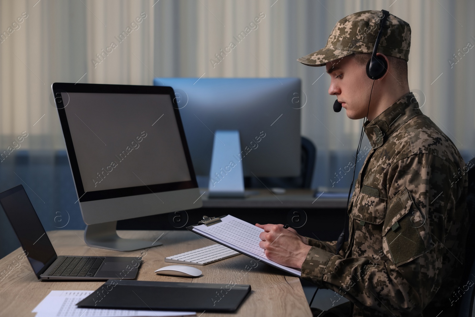 Photo of Military service. Young soldier with clipboard and headphones working at table in office