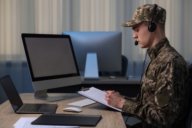 Photo of Military service. Young soldier with clipboard and headphones working at table in office