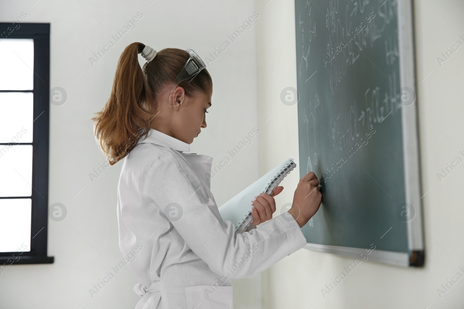 Photo of Schoolgirl writing chemistry formula on blackboard in class