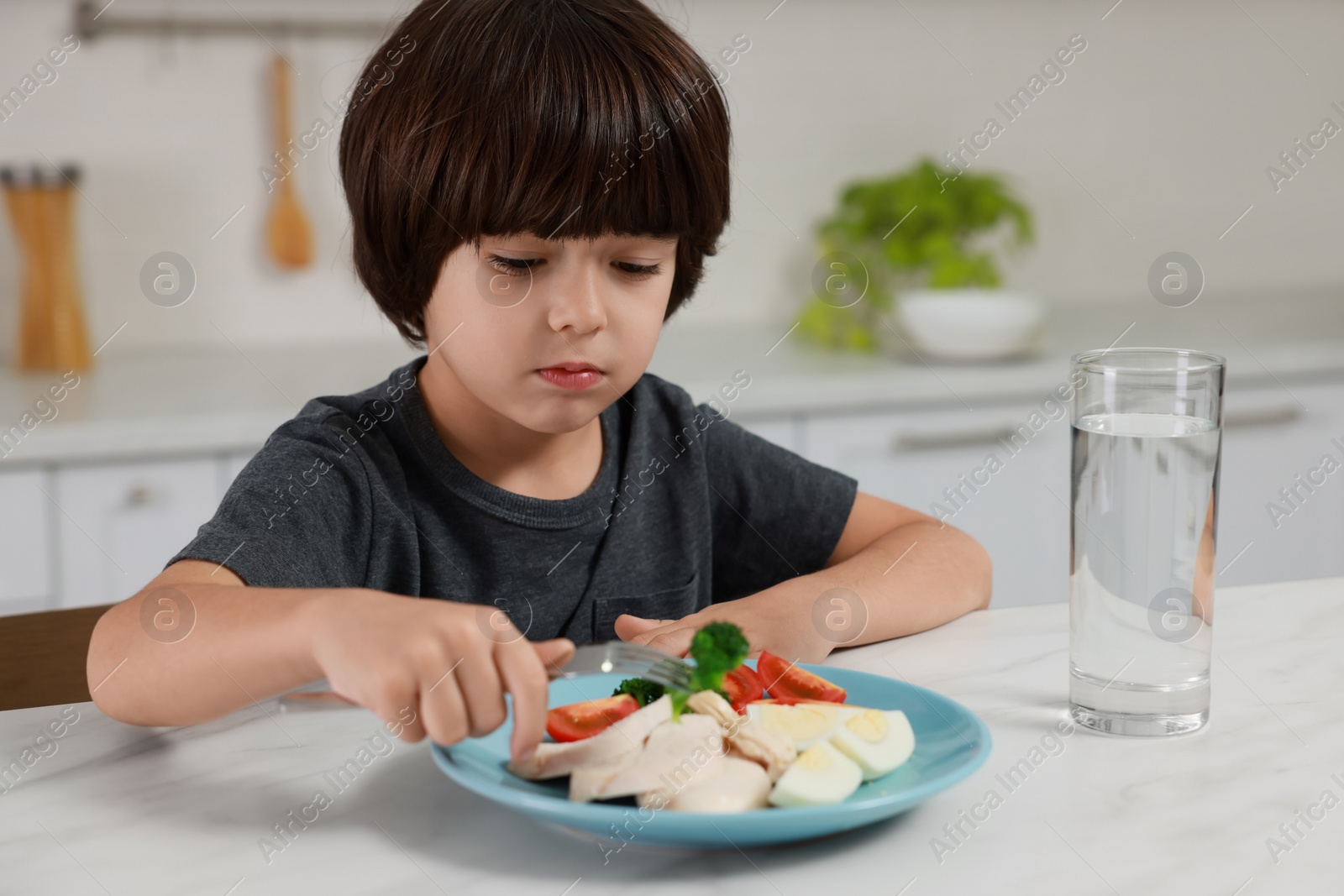 Photo of Cute little boy refusing to eat dinner in kitchen