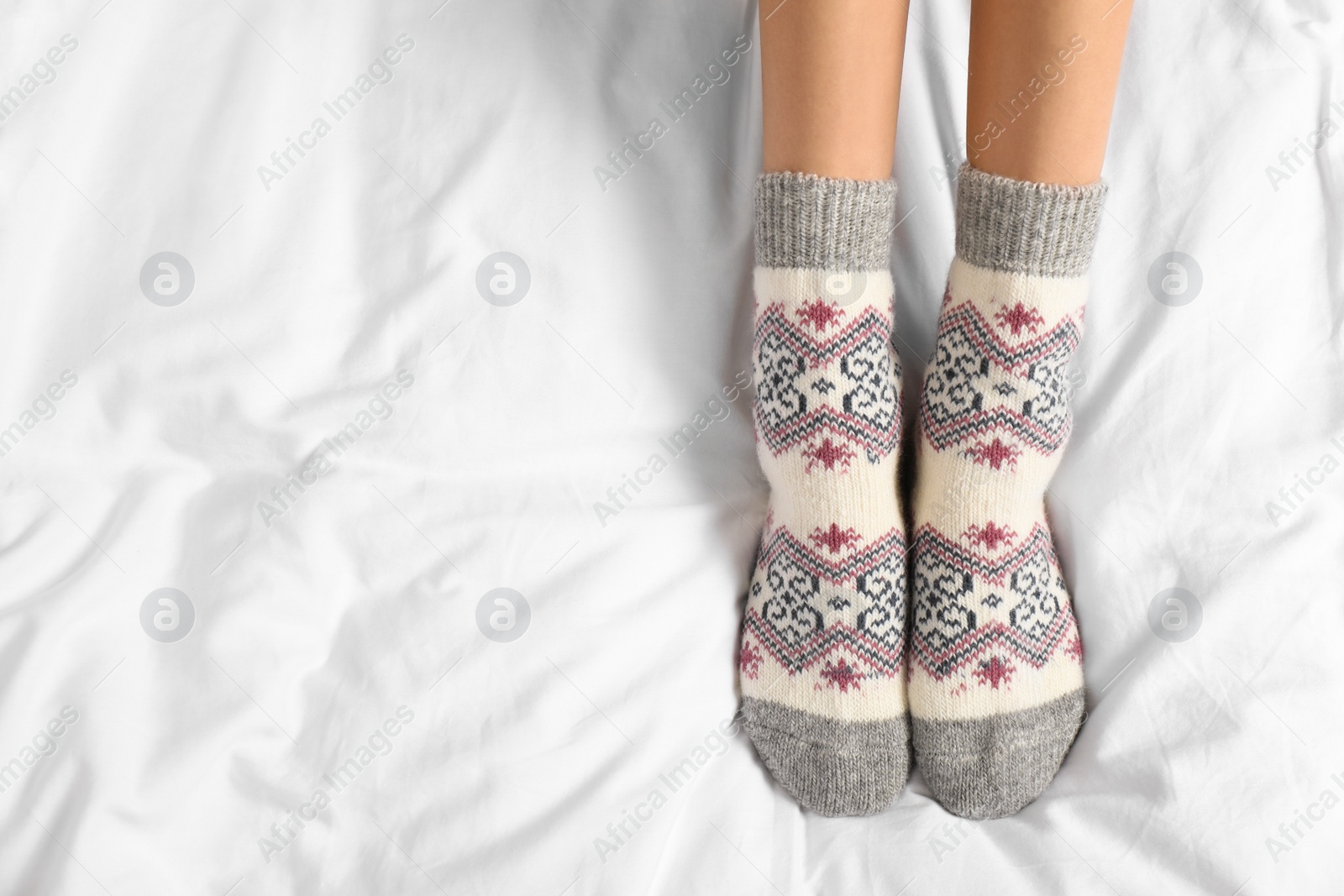 Photo of Woman wearing knitted socks on white fabric, top view with space for text. Warm clothes