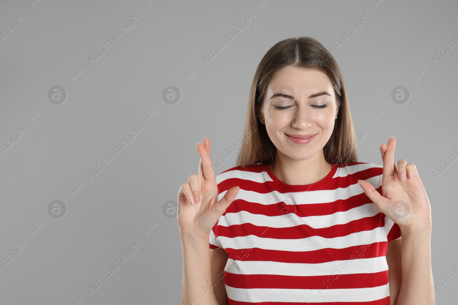 Photo of Woman with crossed fingers on grey background, space for text. Superstition concept