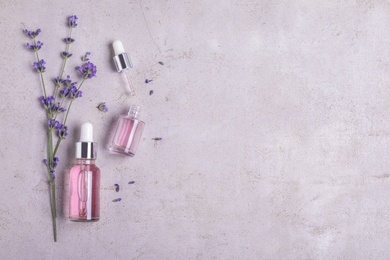 Bottles of essential oil and lavender flowers on stone background, flat lay. Space for text