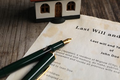 Photo of Last Will and Testament with fountain pen and house model on wooden table, closeup