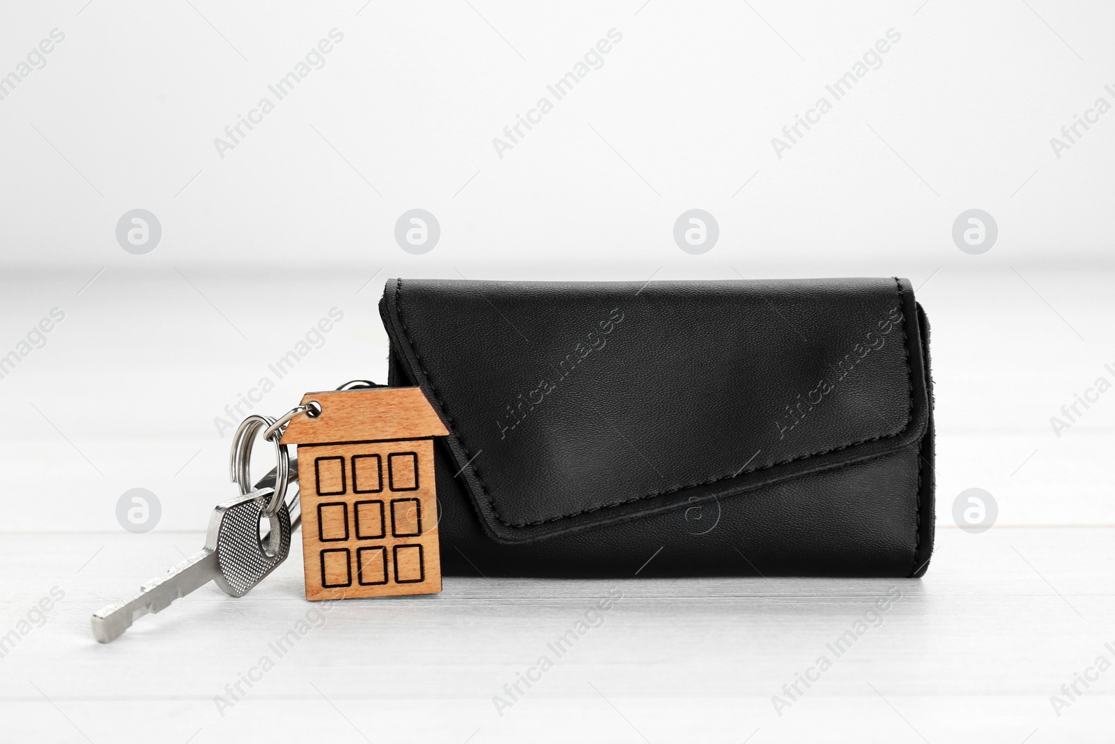 Photo of Leather case with key on white wooden table, closeup