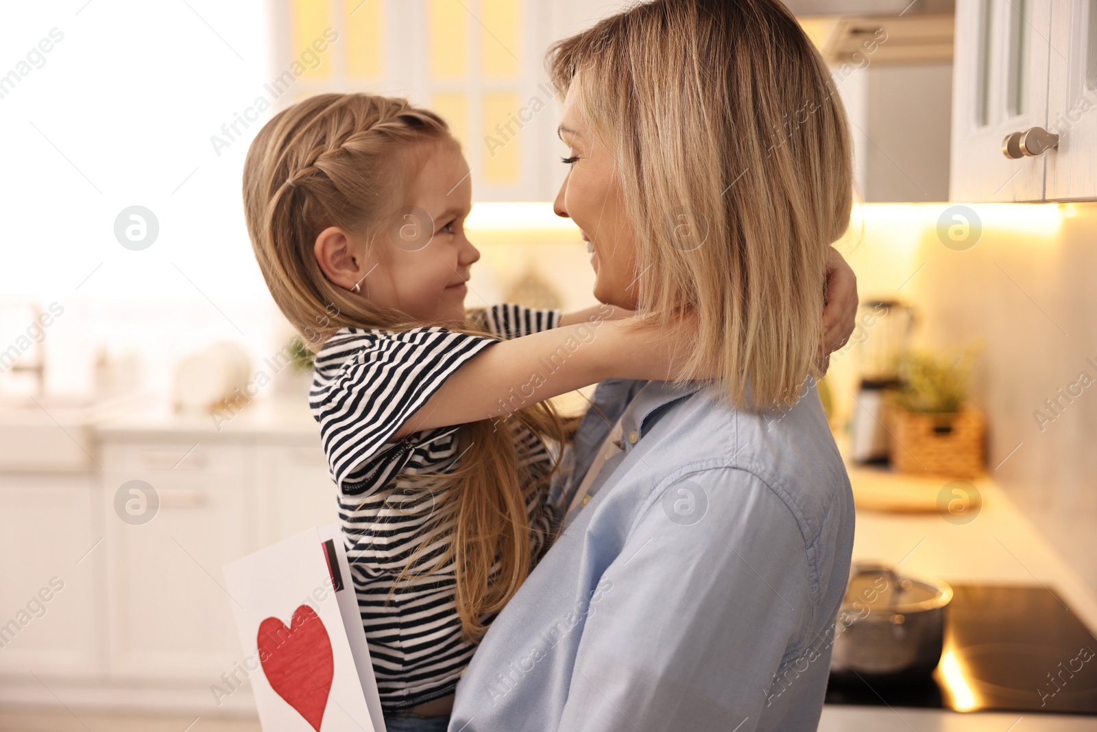 Photo of Little daughter congratulating her mom with greeting card in kitchen. Happy Mother's Day