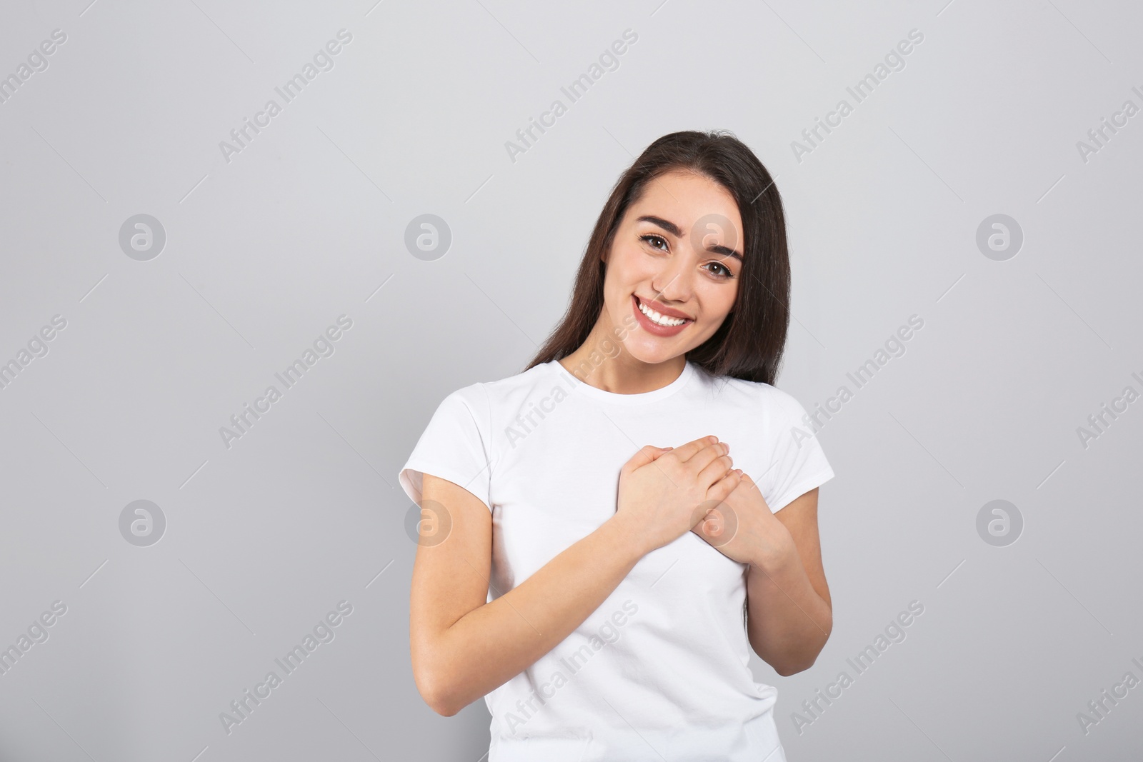 Photo of Beautiful grateful woman with hands on chest against light grey background