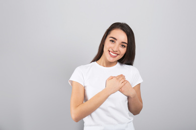 Beautiful grateful woman with hands on chest against light grey background