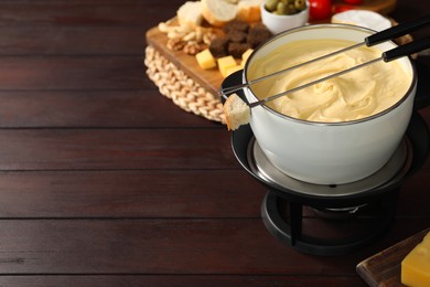 Fondue with tasty melted cheese, forks and different snacks on wooden table, space for text