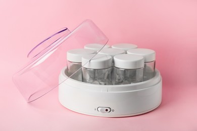 Photo of Modern yogurt maker with empty jars on pink background