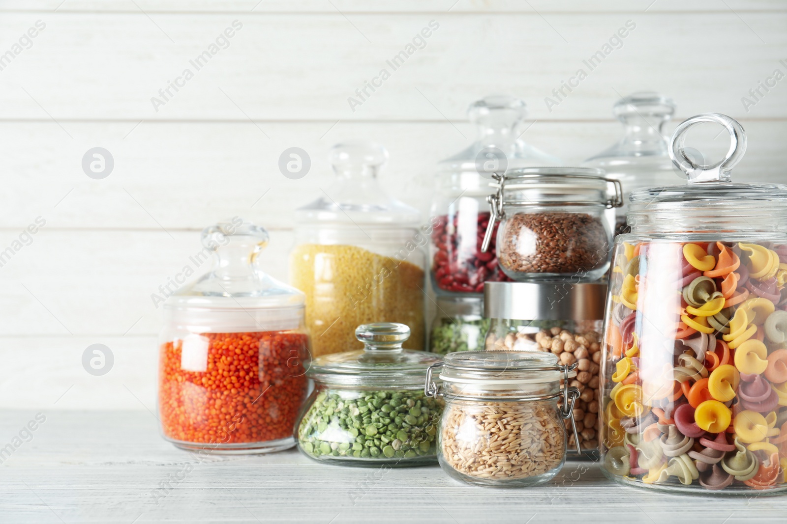 Photo of Glass jars with different types of groats and pasta on white wooden table