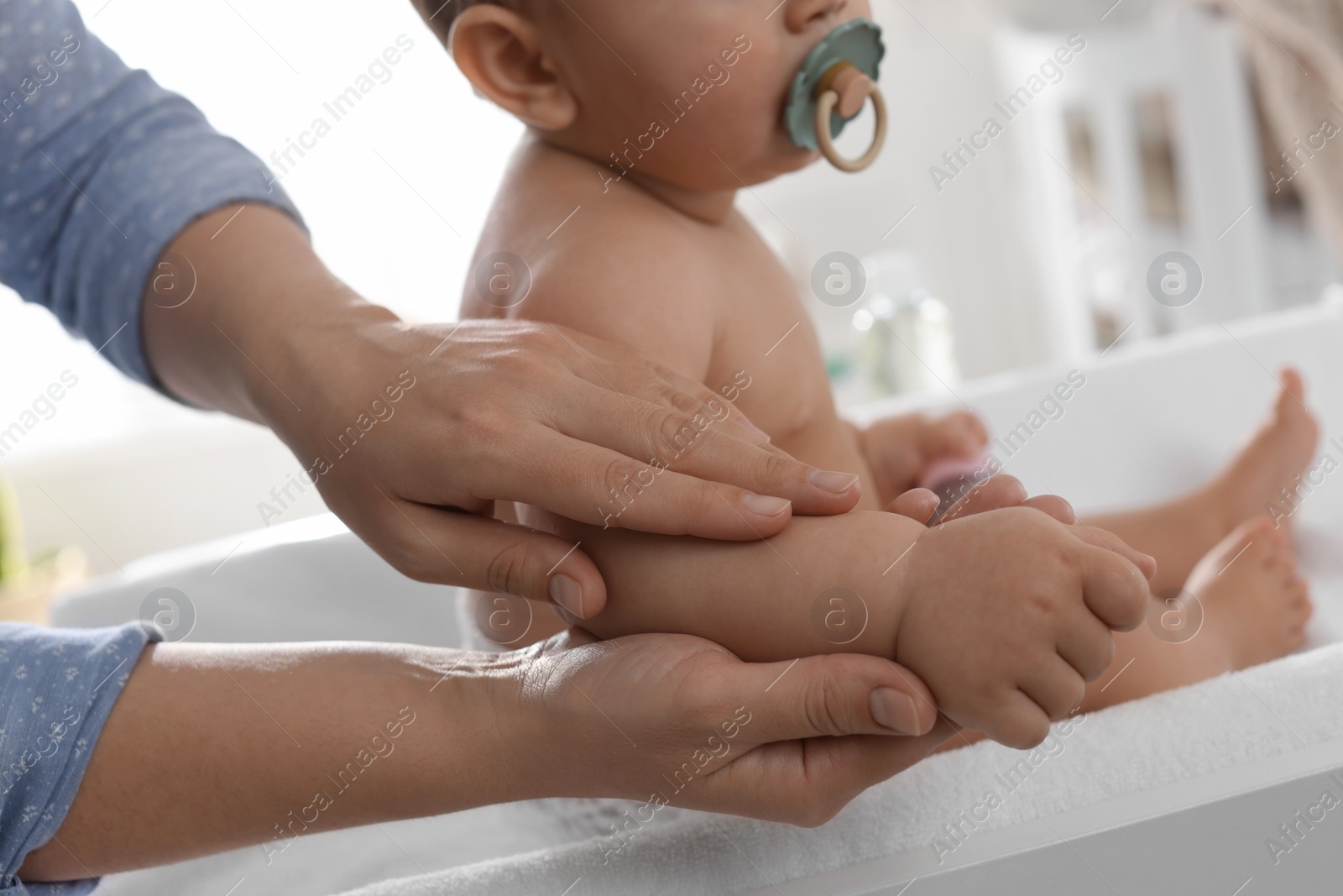 Photo of Mother massaging her baby with oil on changing table at home, closeup