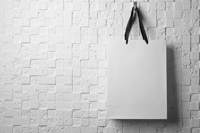 Photo of Paper shopping bag with ribbon handles hanging on white wall. Mockup for design