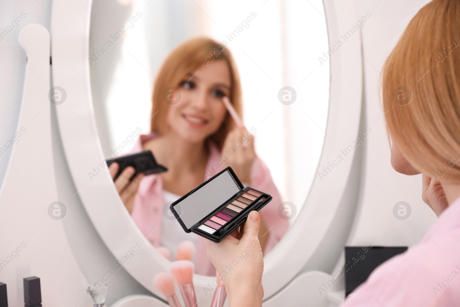Photo of Beautiful young woman applying makeup near mirror indoors, closeup