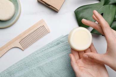 Photo of Woman holding solid shampoo bar at marble table, top view. Hair care