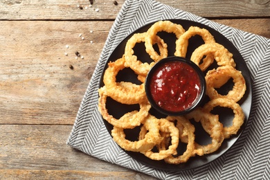 Homemade crunchy fried onion rings with tomato sauce on wooden table, top view. Space for text