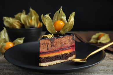 Piece of tasty cake decorated with physalis fruit on wooden table