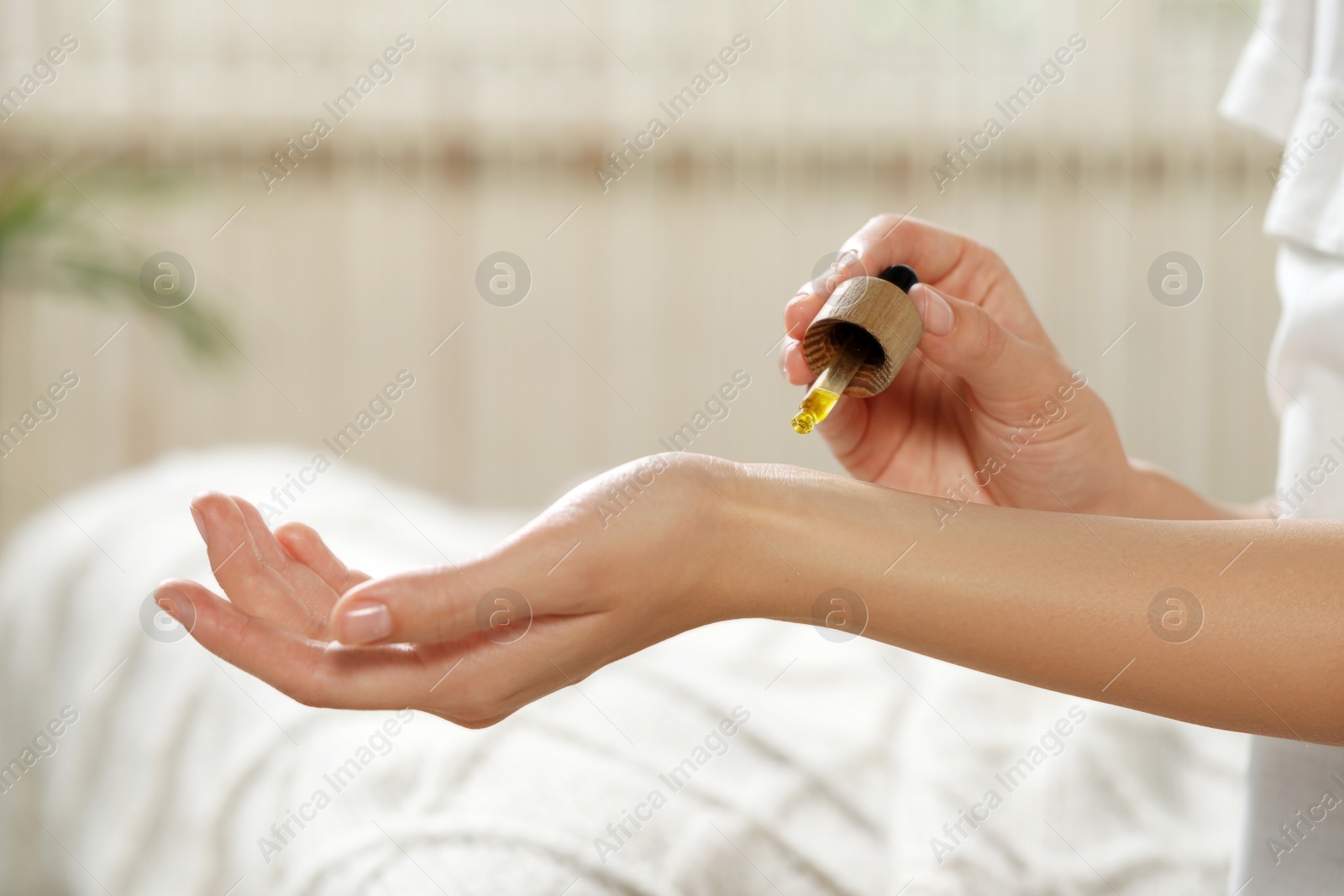 Photo of Young woman applying essential oil onto wrist indoors, closeup