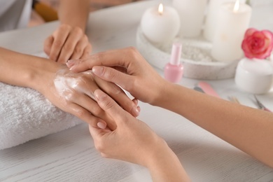 Photo of Cosmetologist applying cream on woman's hand at table in spa salon, closeup