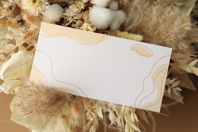 Photo of Blank invitation card and dry flowers on beige background, above view. Space for text