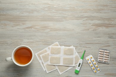 Mustard plasters, pills, thermometer and tea on wooden table, flat lay. Space for text