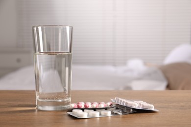 Glass of water and different pills in blisters on wooden table indoors, space for text