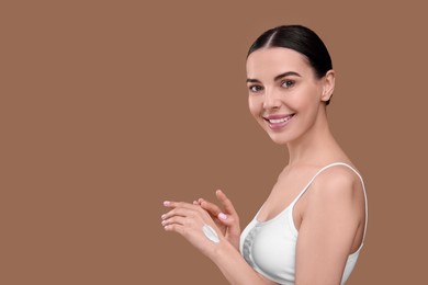 Beautiful woman with smear of body cream on her hand against light brown background, space for text