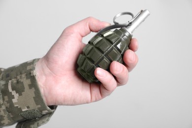 Photo of Soldier holding hand grenade on light grey background, closeup. Military service