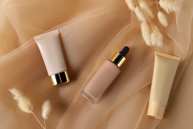 Photo of Skin foundation and dried reeds on beige tulle fabric, flat lay. Makeup product