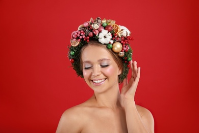 Beautiful young woman wearing Christmas wreath on red background