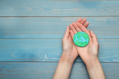Photo of Happy Earth Day. Woman with plasticine planet at turquoise wooden table, top view and space for text
