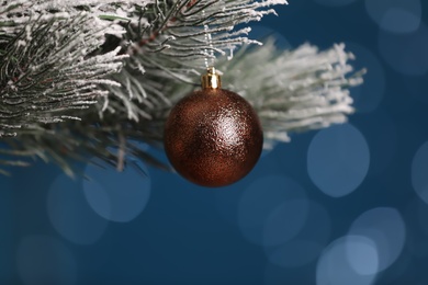Photo of Beautiful holiday bauble hanging on Christmas tree against blue background with blurred festive lights