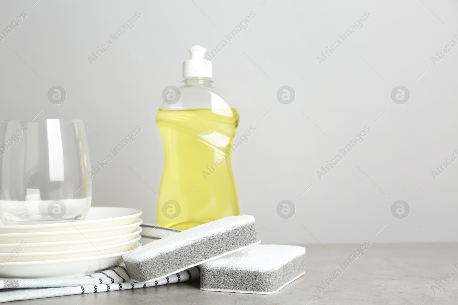 Photo of Cleaning product and sponges near plates on grey table, space for text. Dish washing supplies