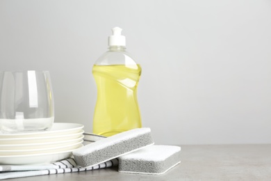 Photo of Cleaning product and sponges near plates on grey table, space for text. Dish washing supplies