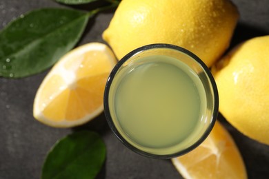 Photo of Tasty limoncello liqueur, lemons and green leaves on grey table, top view