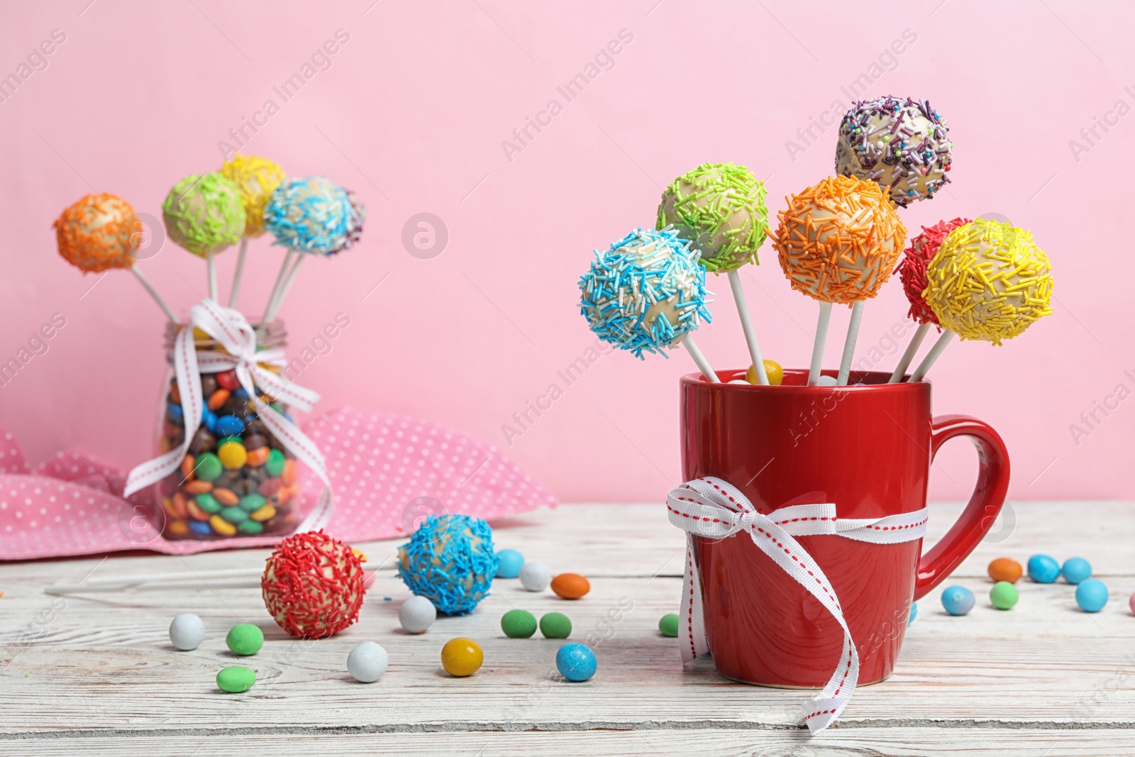 Photo of Cup with tasty cake pops on table, against pink background, space for text