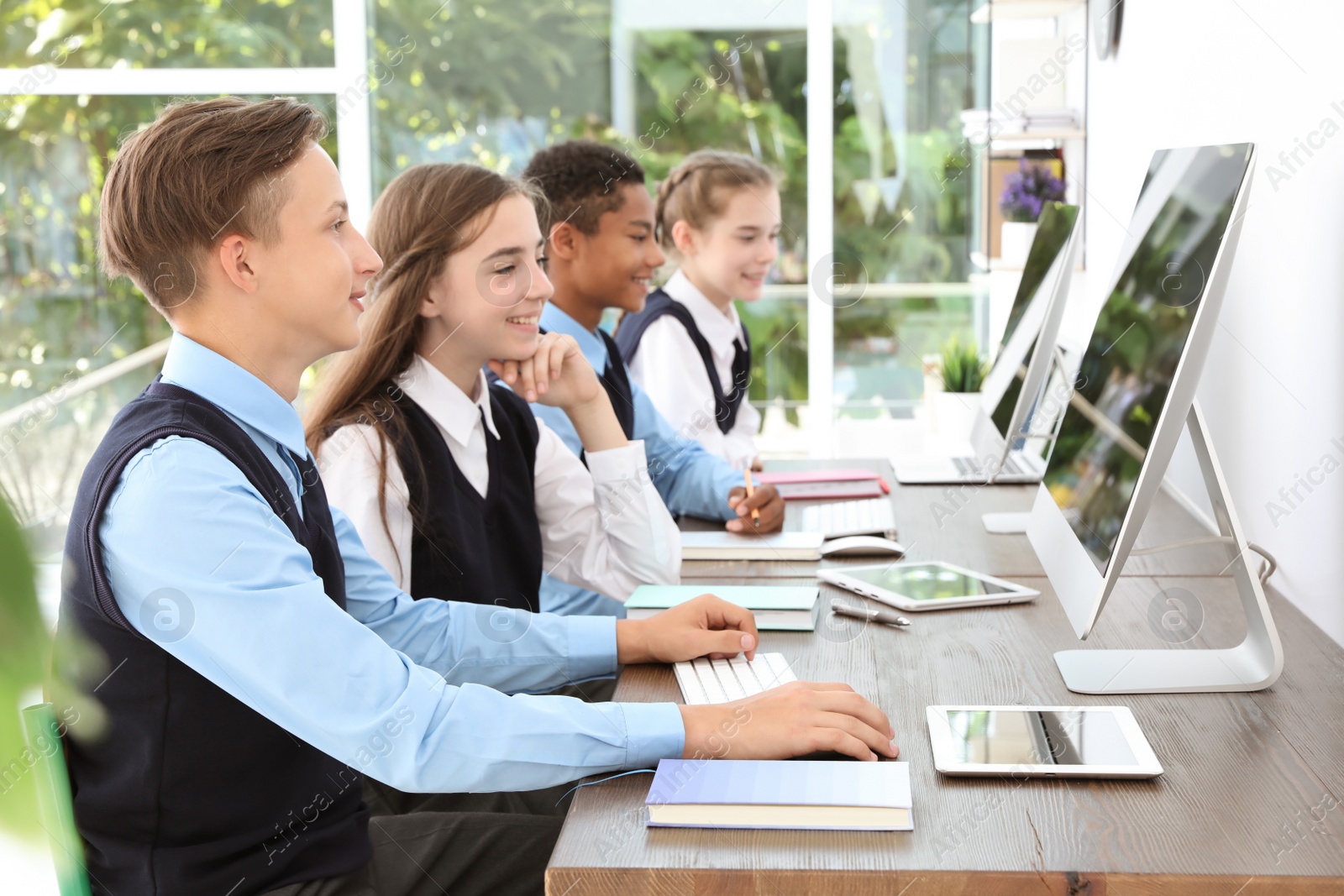 Photo of Teenage students in stylish school uniform at desks with computers