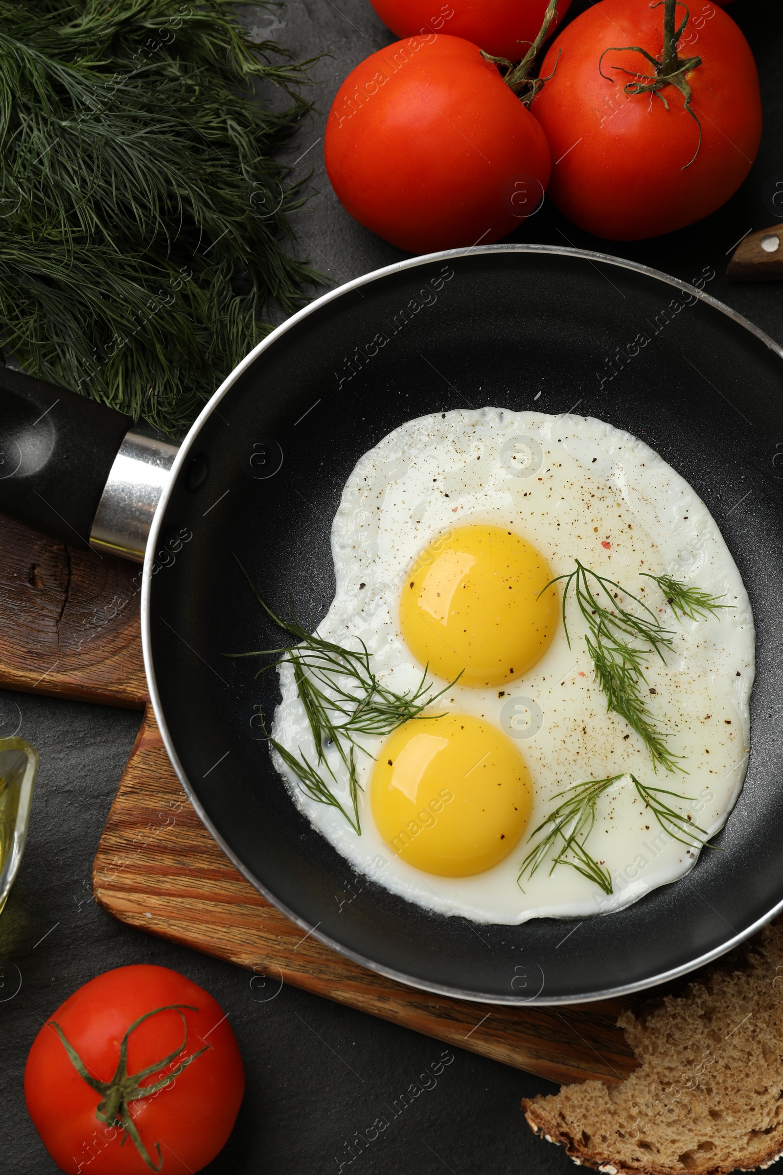 Photo of Frying pan with tasty cooked eggs and other products on black table, flat lay