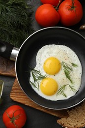 Frying pan with tasty cooked eggs and other products on black table, flat lay