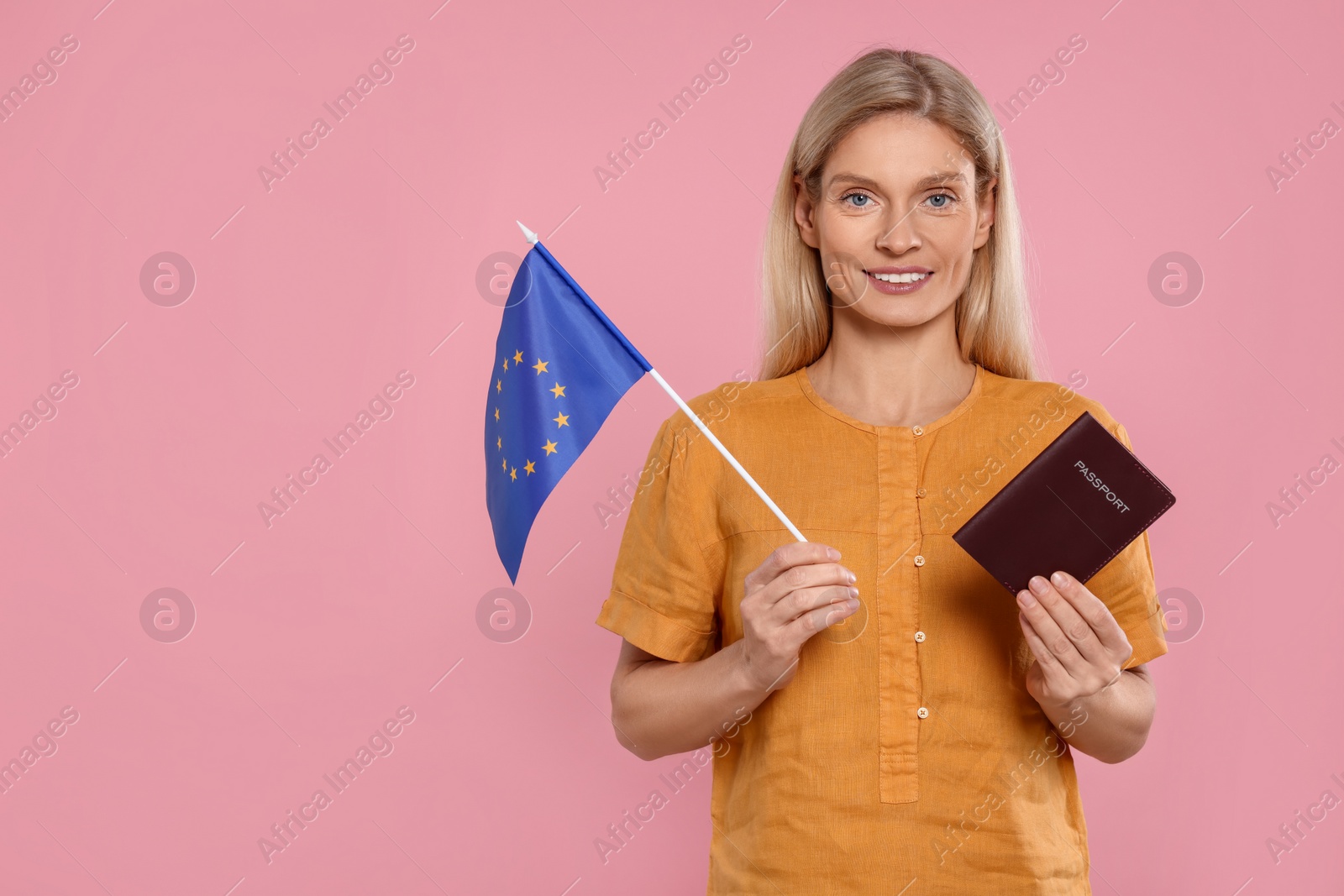 Photo of Immigration. Happy woman with passport and flag of European Union on pink background, space for text