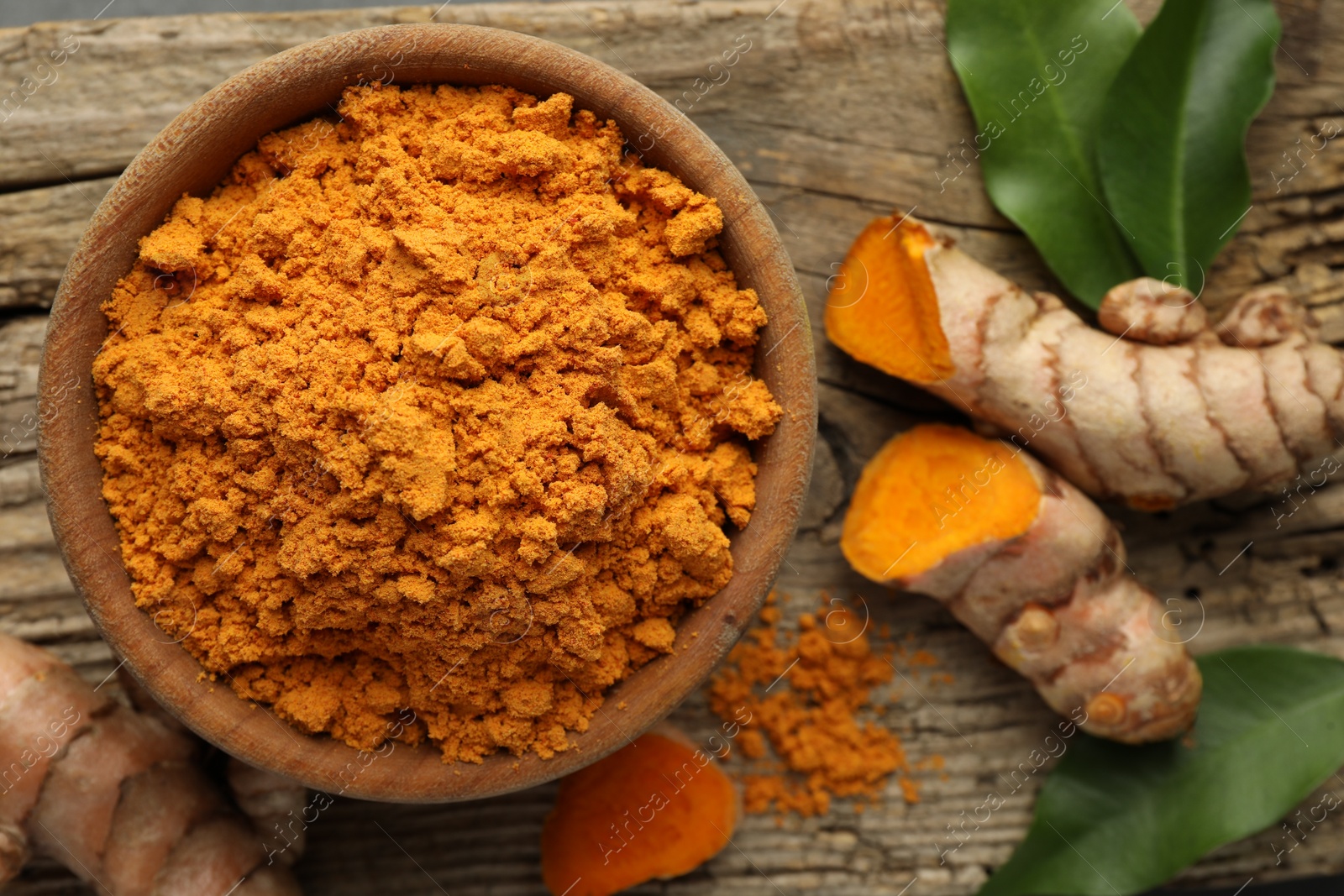 Photo of Aromatic turmeric powder and raw roots on wooden table, flat lay