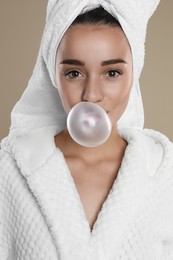 Photo of Young woman in bathrobe blowing chewing gum on brown background