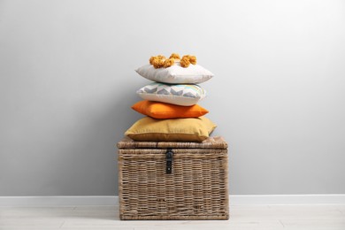 Photo of Soft pillows on wooden trunk near light grey wall indoors