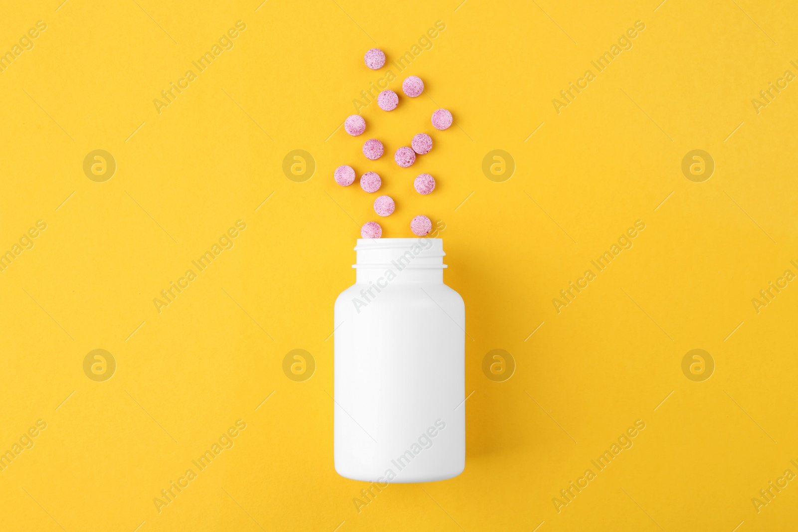 Photo of Bottle and vitamin pills on yellow background, top view