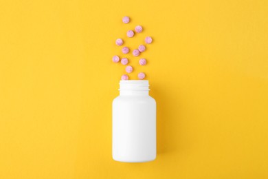 Photo of Bottle and vitamin pills on yellow background, top view